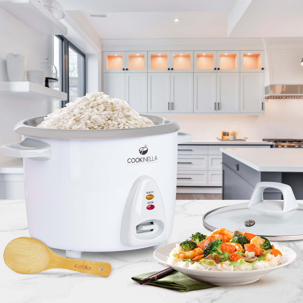Dieser süße Mini Reiskocher KRC-100 mit Edelstahlschüssel steht in einer Küche mit Bambuslöffel und Glasdeckel sowie fertigen Essen.